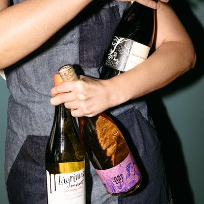 Bartender holding three wine bottles against their chest.