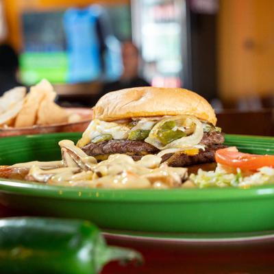 A burger with two patties topped with melted cheese and jalapenos, served with cheese fries.