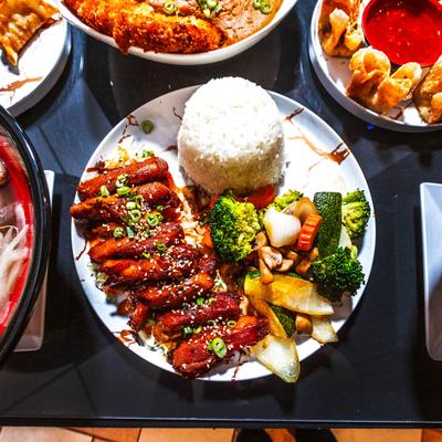 Teriyaki chicken plate accompanied with other food plates on a table, top down view.