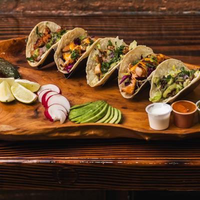 Tacos served with lime, sliced radish, avocado, sour cream, red, and green salsa.