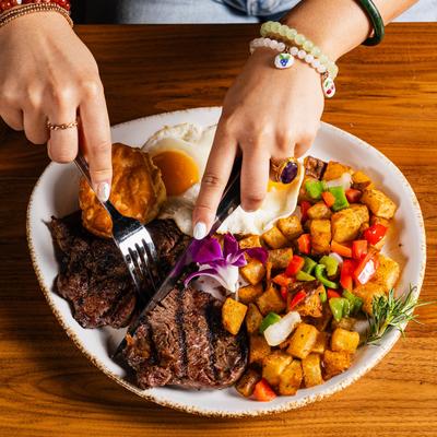 Hands over a meal with steak, eggs, and potatoes.