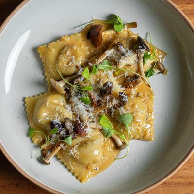 A plate of ravioli topped with grated cheese, mushrooms, and microgreens on a wooden table