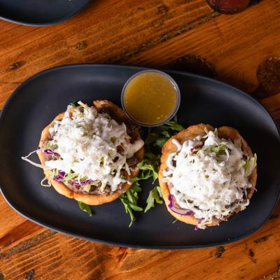 Two sopes topped with steak, arugula, and cotija cheese, served with salsa.