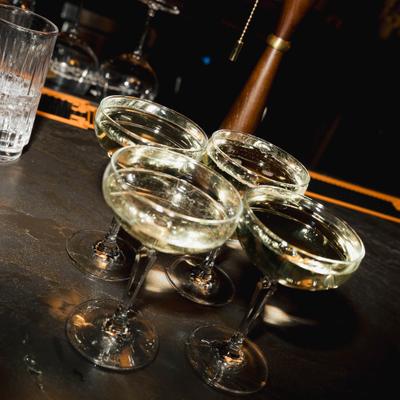 Four champagne glasses filled with sparkling wine sit on a dimly lit bar counter.