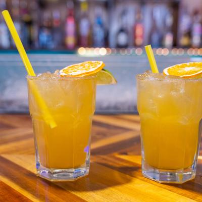 Two citrus cocktails with ice and orange slices served at a bar.