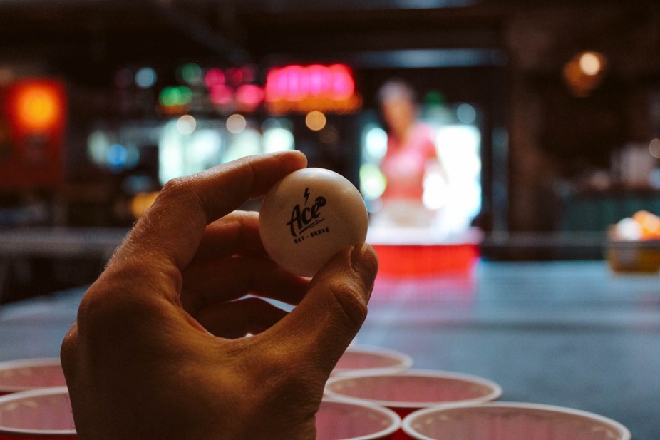 Interior, a person holds a ping pong ball in front of a table.