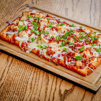 BBQ Chicken Flatbread served on a wooden board atop a wooden table.