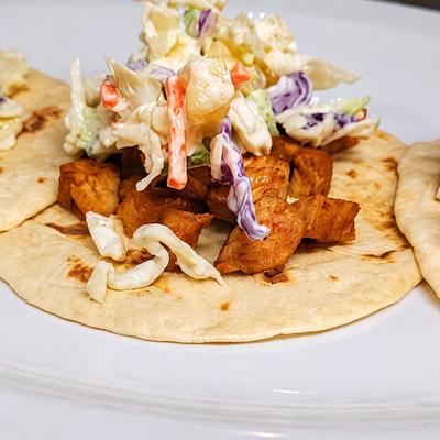 Three tacos topped with slaw and sauce on a white plate..
