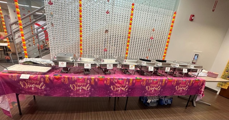 Buffet table set for Diwali celebration, with multiple chafing dishes, trays, and plates