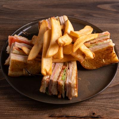 Triple club sandwich with fries, served on a dark plate.