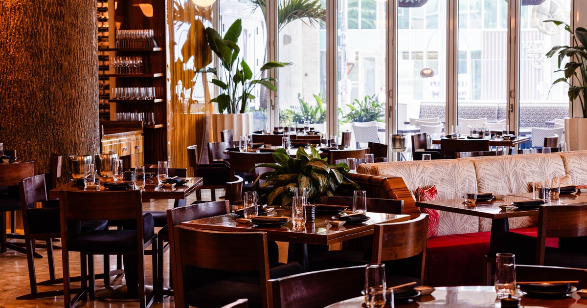 A modern interior - wooden tables set for dining, potted plants; large windows