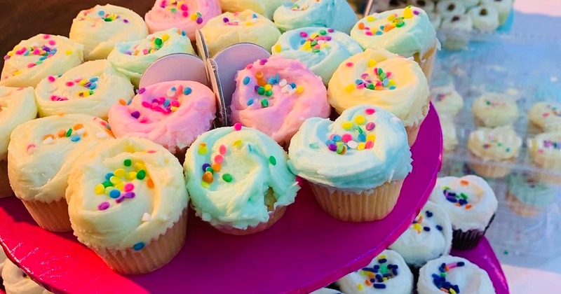 A tiered cupcake stand displays pastel-frosted cupcakes with colorful sprinkles