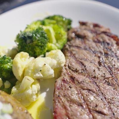Grilled steak served with steamed broccoli and cauliflower.