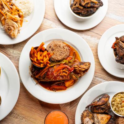 Caribbean spread with fried fish, rice, fries, oxtail, jerk chicken, and drinks.