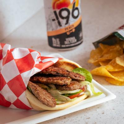 Gyro pita sandwich alongside potato chips and canned drink.