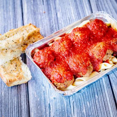 Meatballs covered in marinara sauce with pasta in a foil container next to garlic bread.