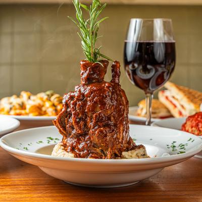 Lamb shank garnished with rosemary sprig accompanied with red wine.