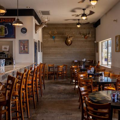 Interior with a bar, tables, chairs, and deer mounts on a wooden wall.