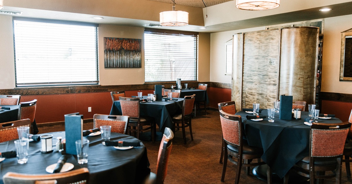 Interior of a restaurant with round tables covered in black tablecloths, wooden chairs