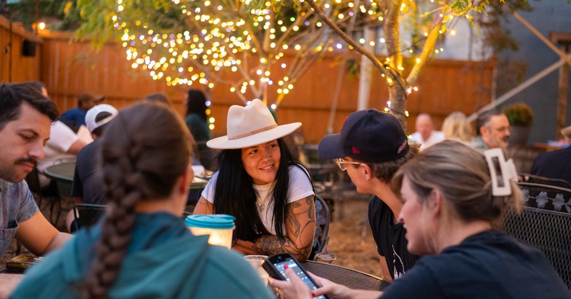 People gathered around a patio table in a warmly lit outdoor setting