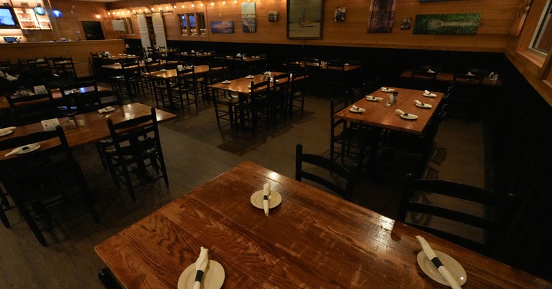 Interior of a dimly lit restaurant with wooden tables, black chairs and wall art.