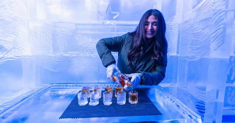 A bartender smiles while pouring drinks into ice glasses inside Alamo Ice Bar