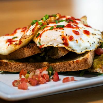 Avocado Toast, with salsa, over easy eggs, arugula, and sriracha.