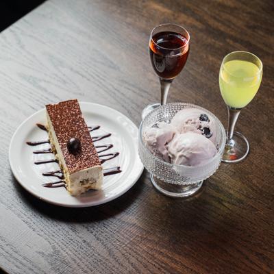 Tiramisu served alongside a cup of ice cream and two glasses with digestif spirits.