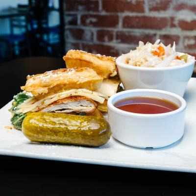 French toast chicken sandwich with a pickle, dipping sauce, and coleslaw on a plate.