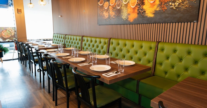 Restaurant interior with green banquette seating, wooden tables set with plates