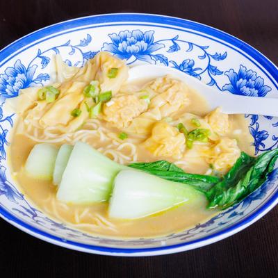 Wonton noodle soup with bok choy in a blue floral bowl.