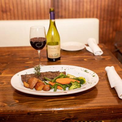 Steak served with roasted potatoes and veggies, accompanied with red wine.