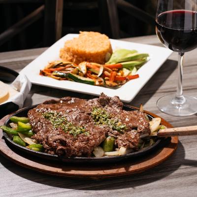 Carne Asada with side vegetables and rice, accompanied with red wine.