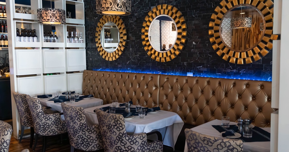 Restaurant interior with gold-framed mirrors, tufted banquette and patterned chairs.