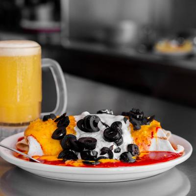 Burrito topped with sour cream and olives, served with a beer.