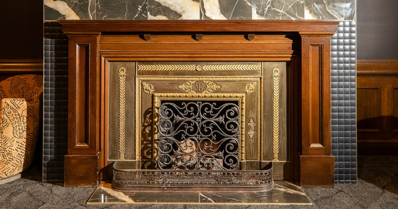 Interior, classical, dark wood fireplace mantelpiece with intricate gilded metal detailing and a decorative iron screen