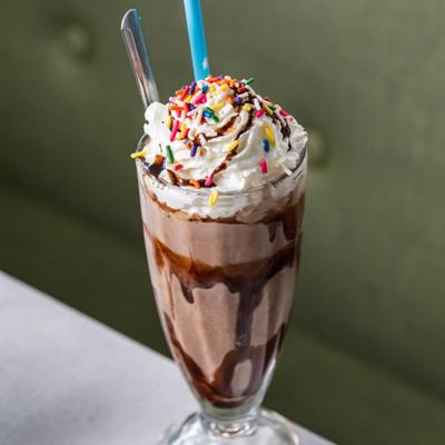 A glass of chocolate milkshake with whipped cream and rainbow sprinkles.