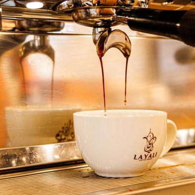 An espresso being brewed into a white ceramic cup with the name Layali.