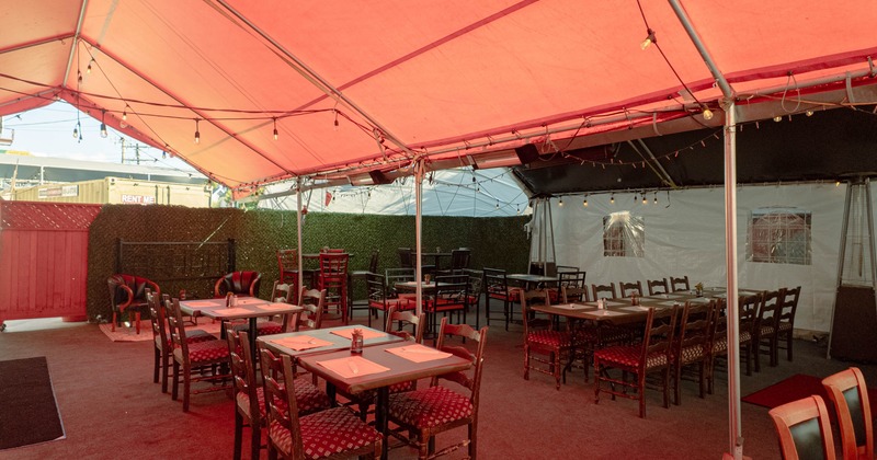 Outdoor dining area under a red tent with wooden tables and chairs