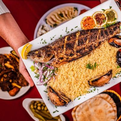 Hands holding the grilled bronzini meal and other meals on the table underneath.