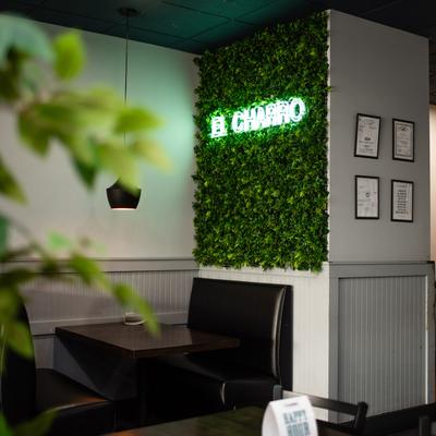 A nook with booth and faux greenery wall with El Charro light sign.