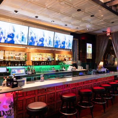 A bar featuring TV screens and several bar stools arranged along the counter.