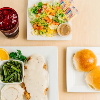 Chicken fried steak with white gravy, green beans, salad, and rolls.