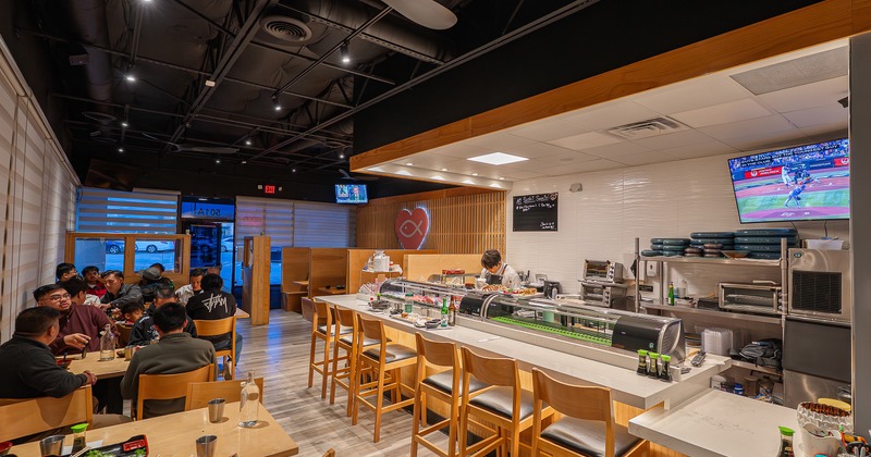 Sushi restaurant interior with an open kitchen and a long counter with chairs along the sushi bar