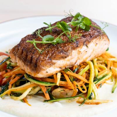 Seared salmon on spiralized vegetables with creamy sauce, garnished with microgreens.