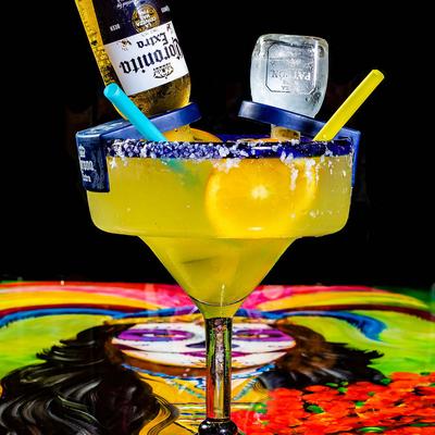 Cocktail in margarita glass with small bottles of beer and tequila inserted into it.