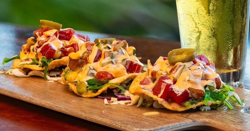 Ahi Poke Tostadas served on a wooden board, with a glass of beer