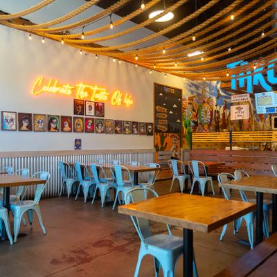 Vibrant Mexican eatery featuring neon signs, rope ceiling accents, and blue industrial chairs.