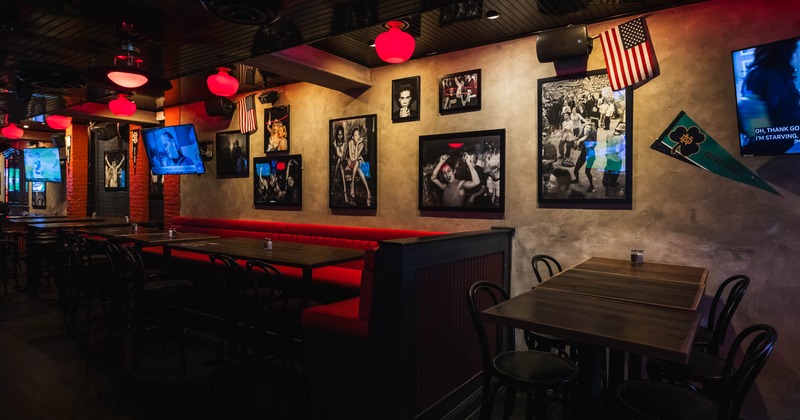 Dimly lit restaurant dining area with red booths, red pendant lights, framed photographs, televisions