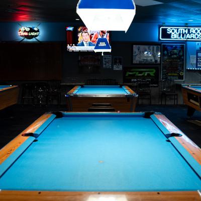 Multiple billiards tables with bright blue felt in a dimly lit bar setting.